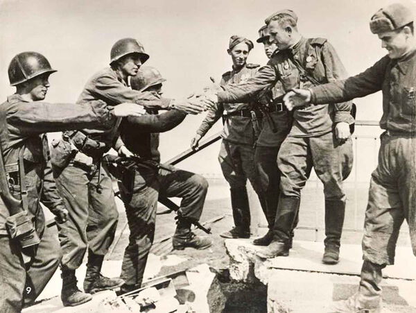 Amerikanische und sowjetische Soldaten reichen sich die Hände auf der zerstörten Pontonbrücke über die Elbe bei Torgau.